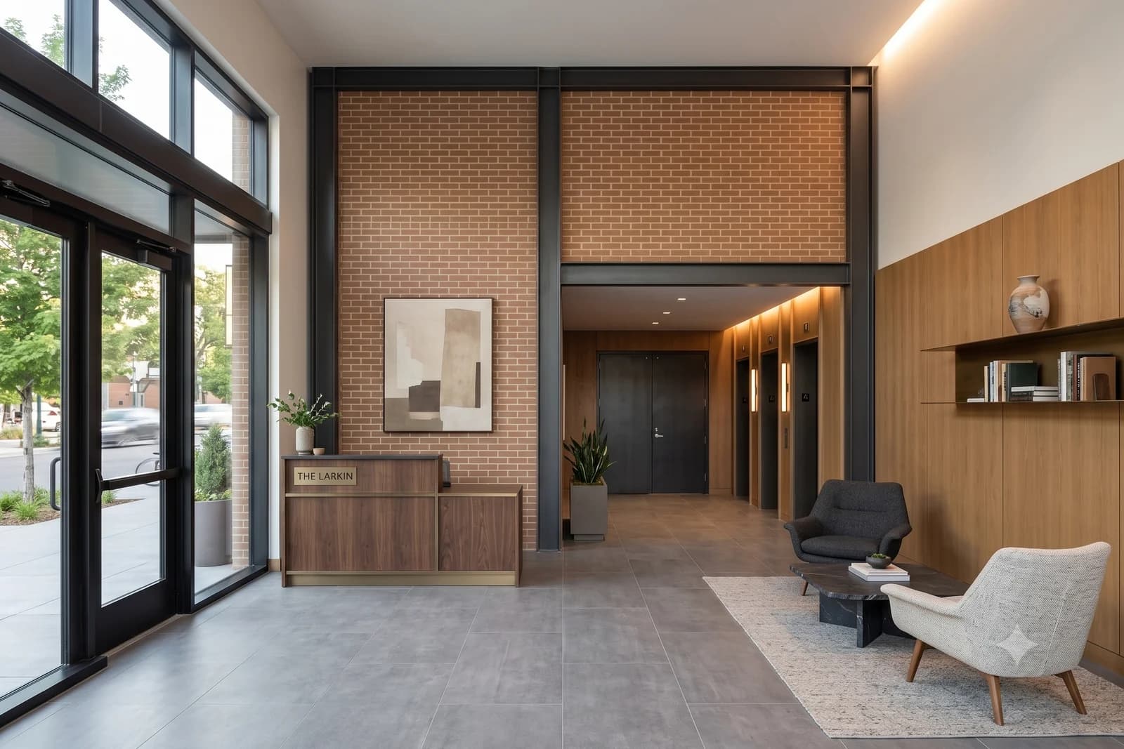 The double-height lobby, exposed brick and black steel columns with a walnut reception desk, a lift bank down the corridor and armchairs on a rug by the window