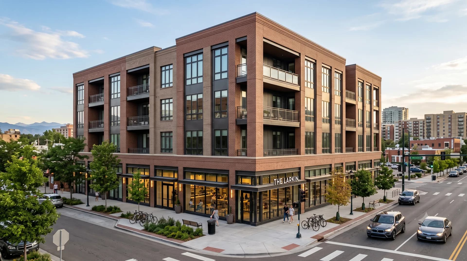 The Larkin from the street corner, four brick residential floors with recessed balconies above a glazed retail frontage, mountains low on the horizon